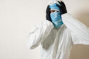 un hombre asustado con un traje protector colgado con máscaras médicas representa el horror contra una pared blanca. los horrores de la epidemia, el peligro del coronavirus foto