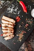 pork cooked in a pan and cut into pieces with spices on a dark stone background photo