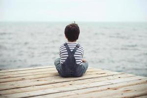 niño pensativo sentarse en el paseo marítimo foto