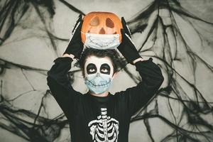 feliz Halloween. niño con máscara médica disfrazado de esqueleto con calabaza de halloween en la cabeza foto