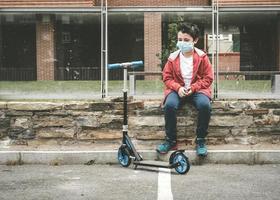 kid wearing medical mask with his scooter in the city photo