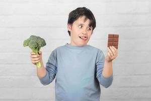 Hungry child with broccoli and an chocolate bar in his hands photo