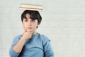 niño pensativo con libros en la cabeza foto