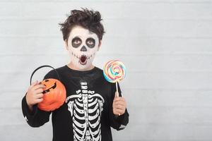 feliz halloween niño divertido en un disfraz de esqueleto comiendo piruleta en halloween foto