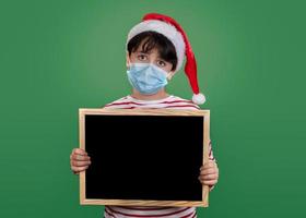 Merry Christmas,funny kid with medical mask holding a blackboard photo