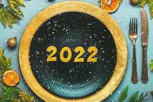 Happy new year 2022. Top view of golden Numbers 2022 on plate for Christmas dinner and snowflakes. New Years Eve celebration concept background photo