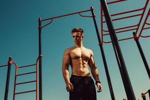 guy with a beautiful athletic body posing while standing next to the horizontal bars photo