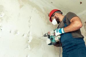 builder with perforator drills holes in concrete wall