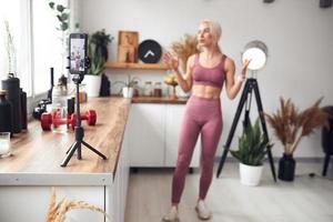 young beautiful blonde takes care of her body while at home during quarantine. She trains people online through her mobile phone photo