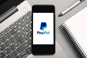 logotipo de paypal en la pantalla negra del teléfono inteligente con computadora portátil y portátil foto