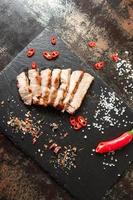 pork cooked in a pan and cut into pieces with spices on a dark stone background photo