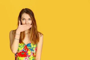 Beautiful girl against yellow wall, closes her mouth with her hand. Concept of female gossip photo
