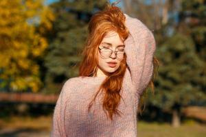 retratos de una encantadora chica pelirroja con una cara linda. chica posando en el parque de otoño con un suéter y una falda de color coral. la niña tiene un estado de ánimo maravilloso foto