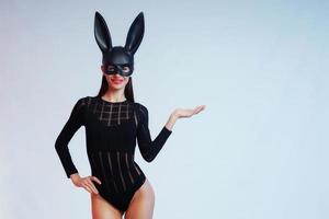 Sexy woman wearing a black mask Easter bunny standing on a blue background and looks very sensually