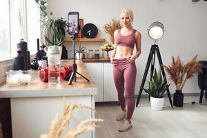 young beautiful blonde takes care of her body while at home during quarantine. She trains people online through her mobile phone photo