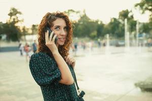 Portraits of a charming red-haired girl with a pretty face. The girl talks cutely with someone on the phone. She has a great mood and a sweet smile photo