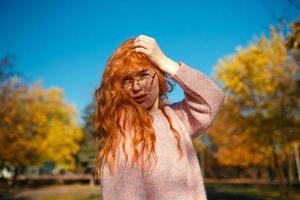 retratos de una encantadora chica pelirroja con una cara linda. chica posando en el parque de otoño con un suéter y una falda de color coral. la niña tiene un estado de ánimo maravilloso foto