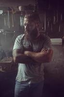 Handsome brutal man with a beard standing in his garage against the background of repair tools photo