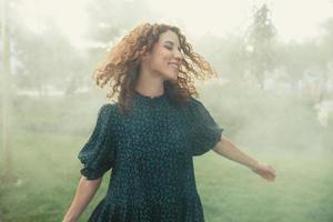 cute red-haired curly girl rejoices under the water fogger in the city center photo