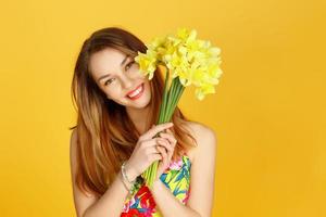 mujer sosteniendo flores amarillas y sonriendo contra la pared amarilla foto