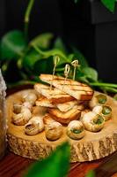 Baked snails with garlic oil and herbs on a wooden plank
