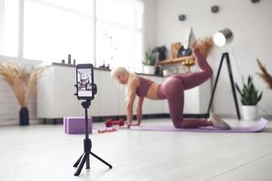 young beautiful blonde takes care of her body while at home during quarantine. She trains people online through her mobile phone photo