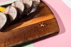 Fresh chopped mackerel lies on a kitchen board along with cod-liver oil capsules photo