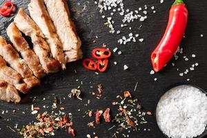 pork cooked in a pan and cut into pieces with spices on a dark stone background photo