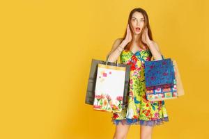 Portrait of young happy smiling woman with shopping bags against yellow wall photo