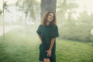 cute red-haired curly girl rejoices under the water fogger in the city center photo