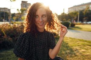 charming curly red-haired girl with freckles in dress poses for the camera in the city center showing different facial emotions photo