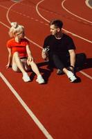young beautiful blonde and a guy are sitting on a jogging track with a bottle of water and chatting photo