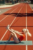 young blonde shakes abdominal muscles on a sports mat on the street photo