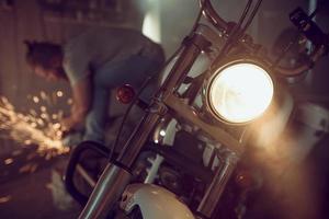 apuesto hombre brutal con barba reparando una motocicleta en su garaje trabajando con una sierra circular. en el garaje muchas chispas y humo de aserrar foto