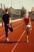 girl and a guy doing a warm-up before sports exercises at the school stadium photo