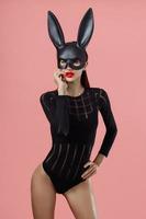 Sexy woman wearing a black mask Easter bunny standing on a pink background and looks very sensually photo
