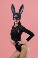 Sexy woman wearing a black mask Easter bunny standing on a pink background and looks very sensually photo