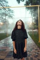 cute red-haired curly girl rejoices under the water fogger in the city center photo