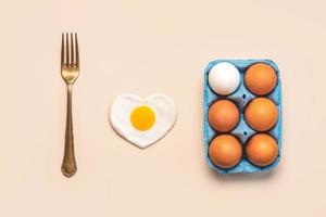 vista superior de los huevos de pollo en una caja de cartón azul abierta con un tenedor vintage y un huevo frito en forma de corazón foto