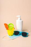 Protective surgical mask with sunglasses,beach bucket and plastic bottle of sunscreen photo