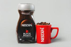 tarro de nescafé asado negro y taza roja de nescafé con granos de café foto