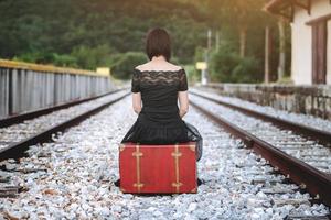 mujer sentada en una maleta en las vías del tren