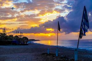 Flags and plane at golden sunset Ialysos Beach Rhodes Greece. photo