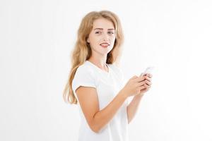 Young beautiful woman in t shirt using her smartphone isolated on white background. Sexy blond girl chating with friend or shopping online. Copy space photo