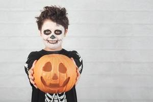 feliz halloween niño divertido en un disfraz de esqueleto con calabaza de halloween foto
