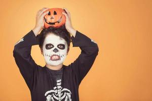 feliz halloween niño divertido en un disfraz de esqueleto con calabaza de halloween sobre su cabeza foto