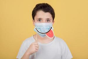 niño con máscara médica y sonrisa falsa en el palo foto