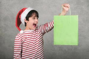 Merry Christmas, smiling kid wearing Santa Claus hat holding a shopping bag photo