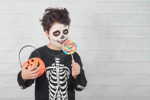feliz halloween niño divertido en un disfraz de esqueleto comiendo piruleta en halloween foto