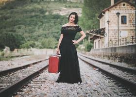 young woman with a red suitcase on the train tracks photo